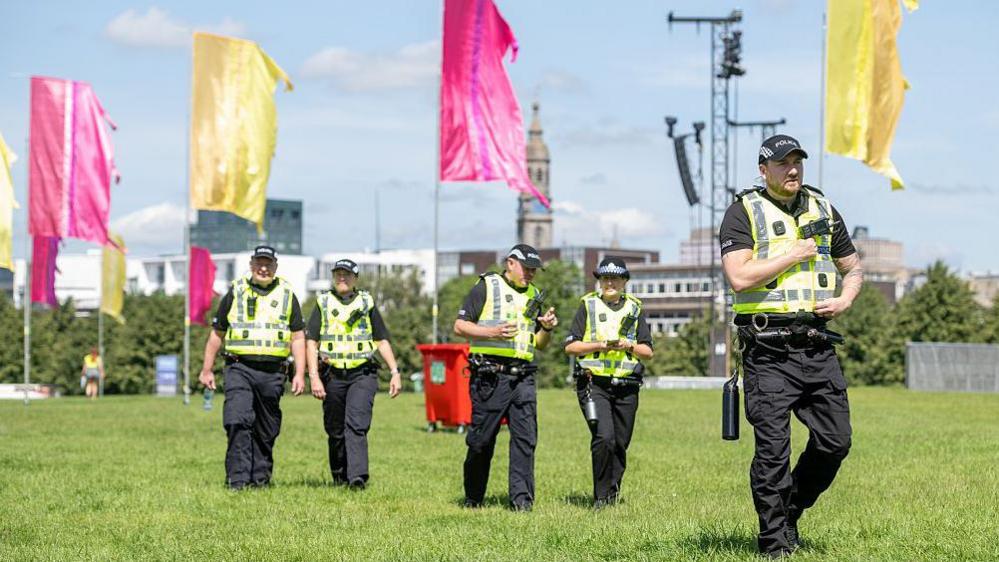 Police officers walking across a grassed area with large flags in the background