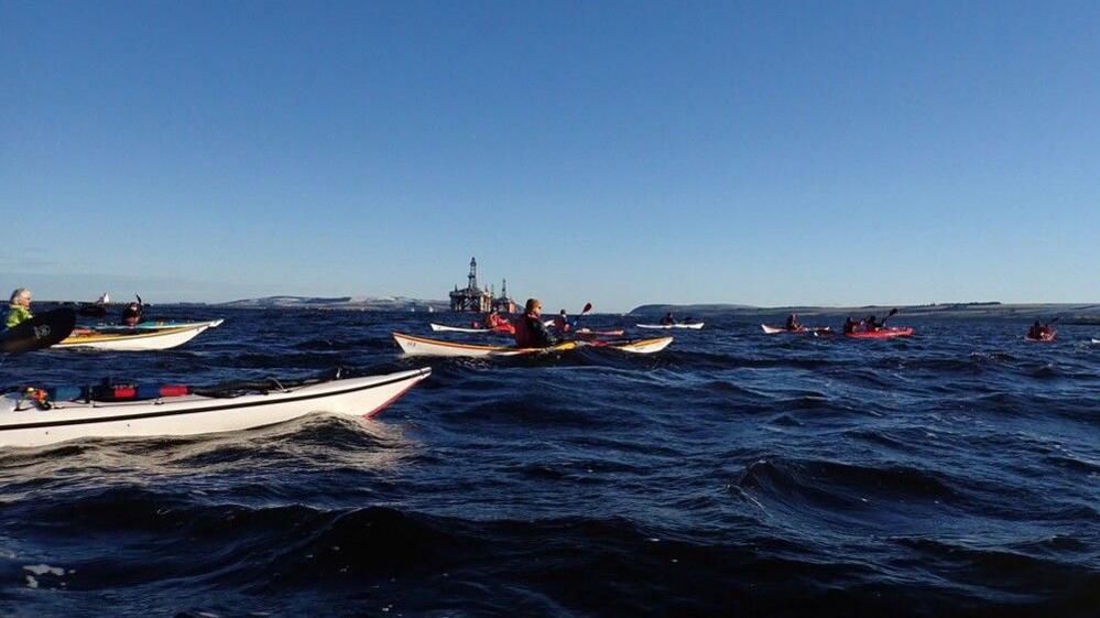 People in kayaks on the Cromarty Firth on a bright day with a blue sky.
