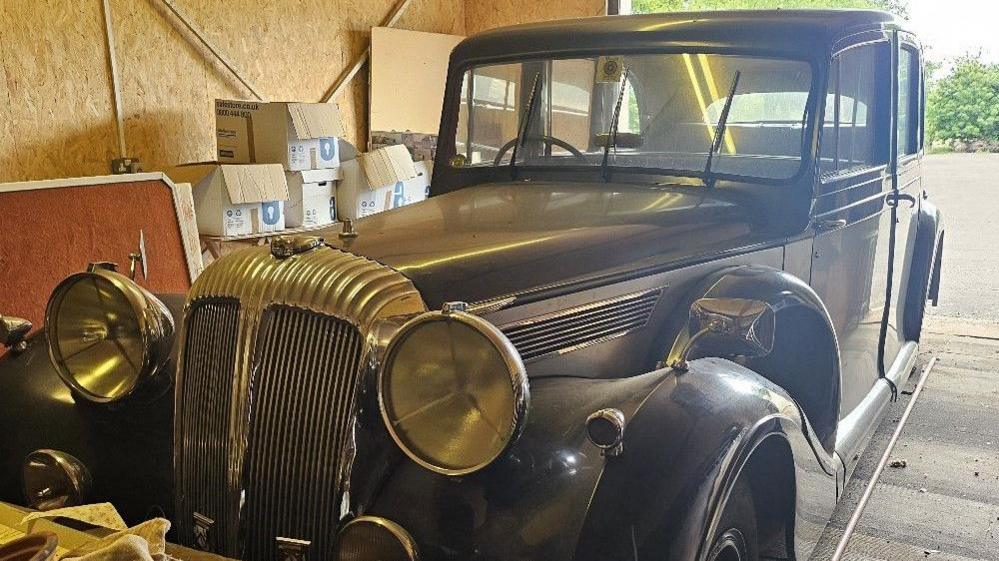 A vintage Daimler vehicle, in a storage unit and surrounded by cardboard boxes.