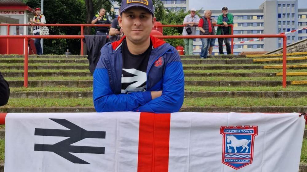  Karim Goodchild standing on some steps with an Ipswich Town flag draped over a railing