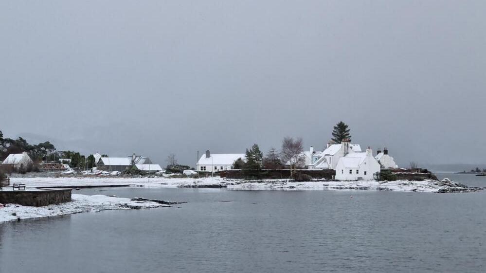 Snow covered houses in a little coastal town surrounded by water on a grey day.