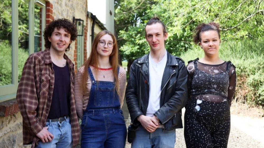 Two young men and two young women standing in row outside building near trees.