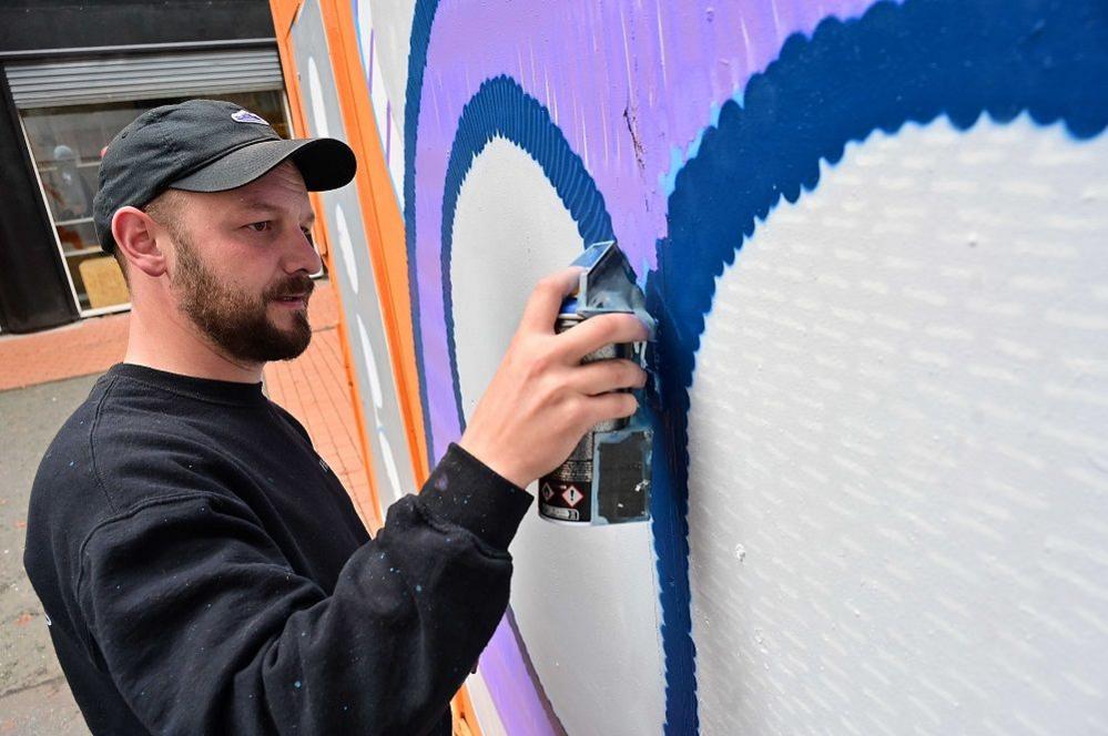 A person in a black cap and black jumper is seen spray painting a wall. 