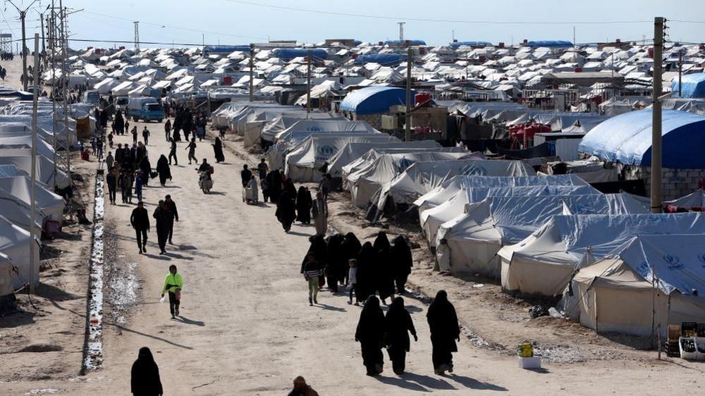 A group of women walks down a path between dozens of tents.