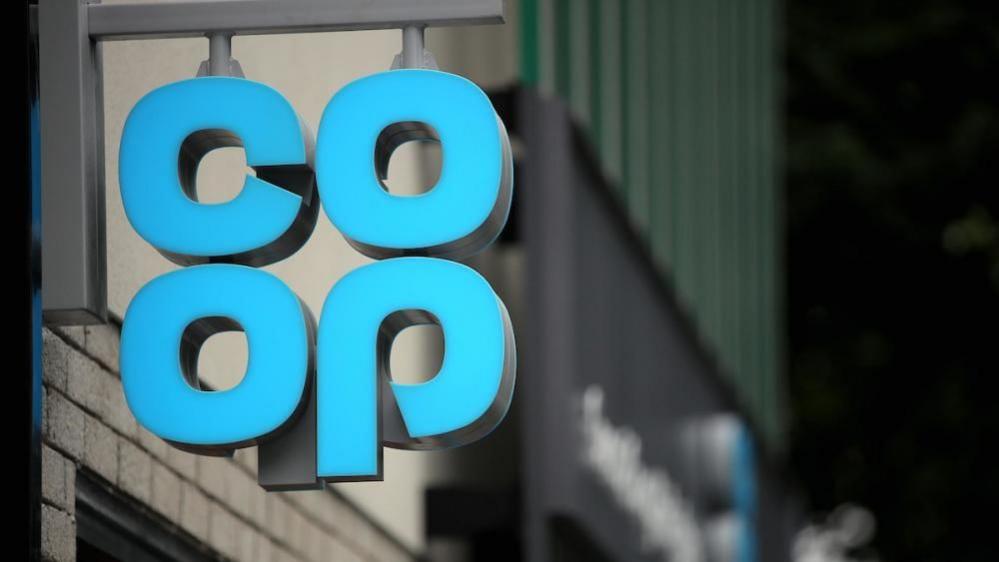 A hanging sign outside a shop showing the pale blue Co-op logo