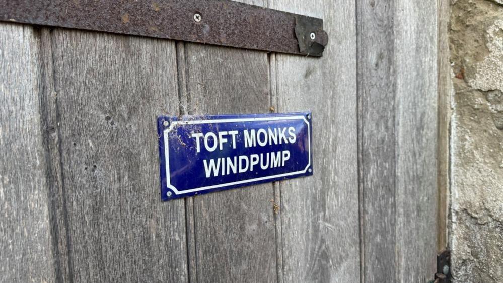 A Parisian-style enamel plaque in blue with white text and border, that states: "Toft Monks Windpump"