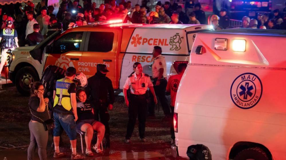 A woman sits on a chair by a group of ambulances