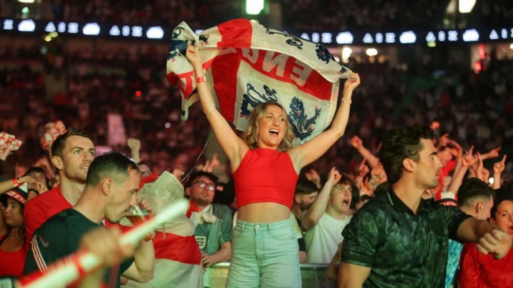 Fans, many in England colours, celebrating a goal with a woman holding a large England flag