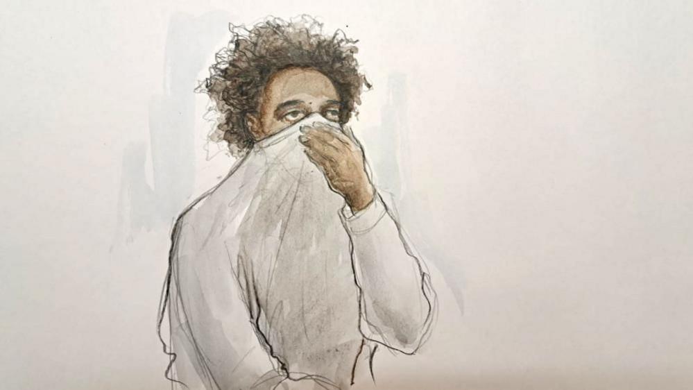 A court sketch of a young man with curly dark hair holding his jumper up over his mouth and nose. 