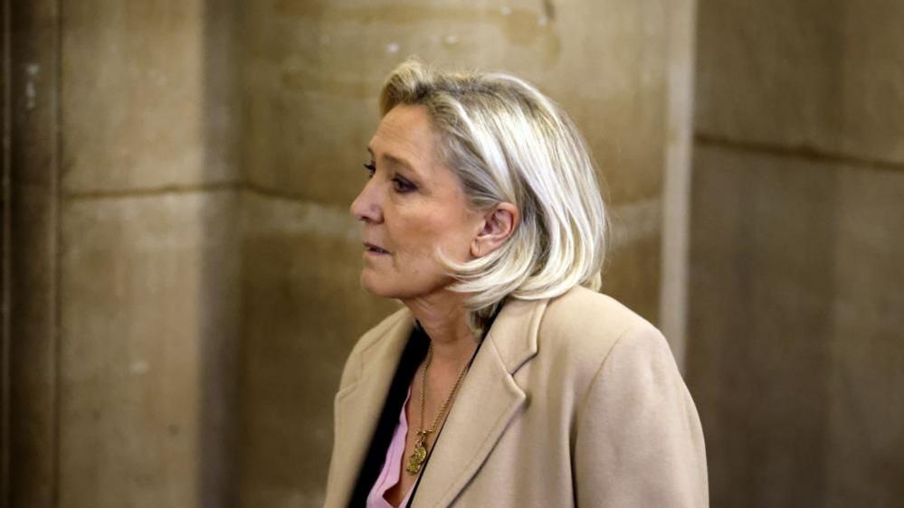 Marine Le Pen arrives at the Appeals Court, wearing a beige coat, pink shirt and a necklace 