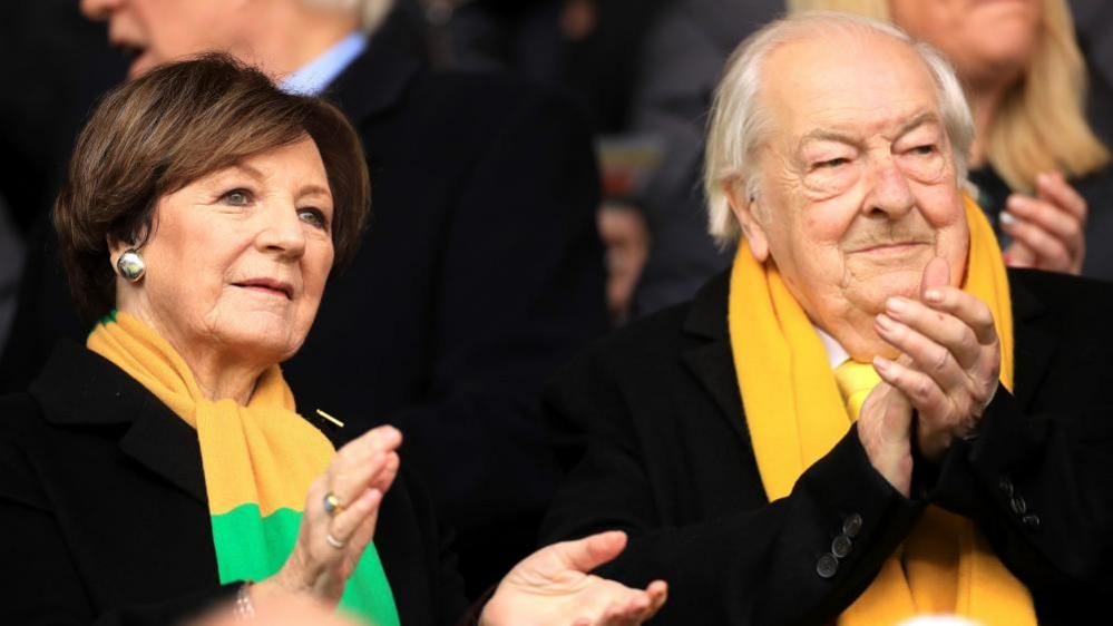 Delia Smith and Michael Wynn Jones wearing Norwich City scarves and clapping