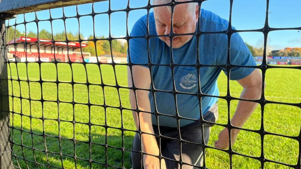 Roger Rose works on a plastic fence on the edge of a football pitch.