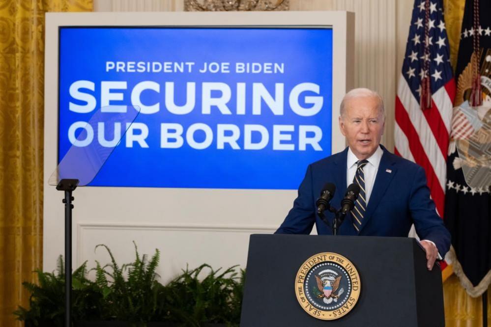 President Joe Biden speaks from a podium with a screen in the background the reads "Securing Our Border"