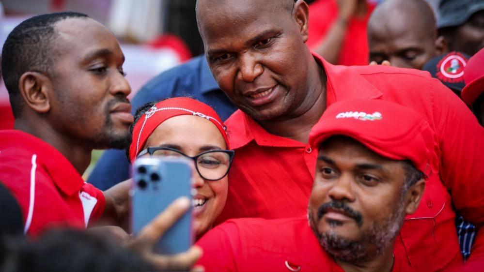 In a red T-shirt, Daniel Chapo poses for a selfie with a smiling woman in Maputo on 23 December 2024