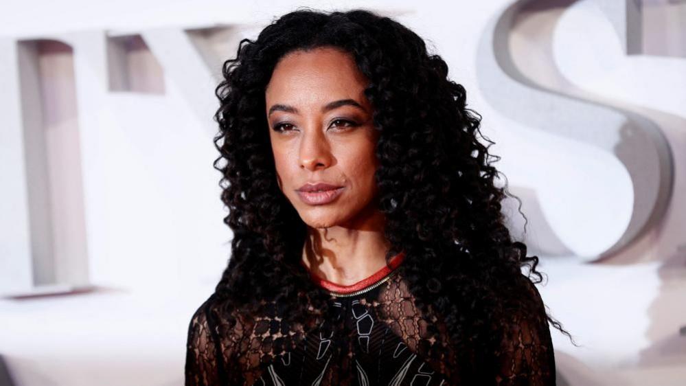 Corinne Bailey Rae with long dark hair standing in front of large letters