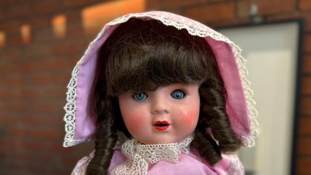 A doll with a pink bonnet and dark brown curly hair.