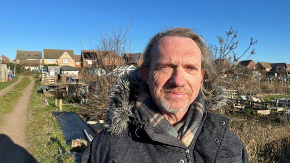 Jonathan Harris in a coat and scarf with long light-colour hair