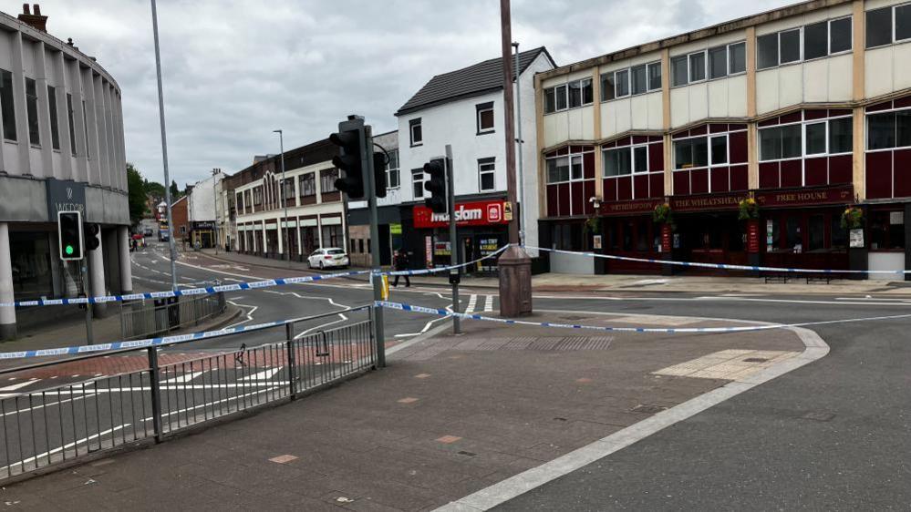 A police cordon in place on a high street in a city centre. The cordon is across a set of traffic lights and blocks multiple roads.