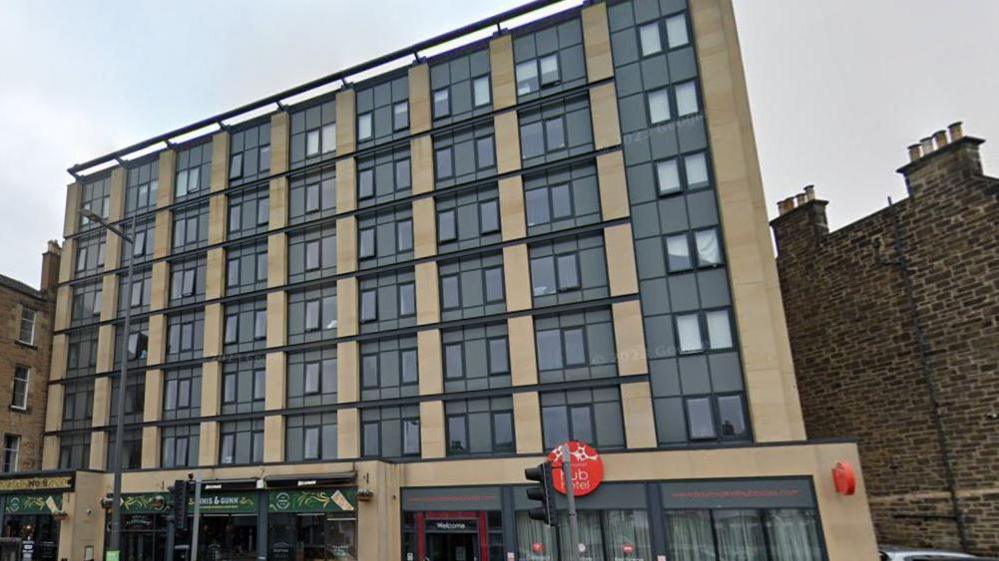 A grab of a modern-looking hotel. It is rectangular with lots of glass and a blonde sandstone effect within each window