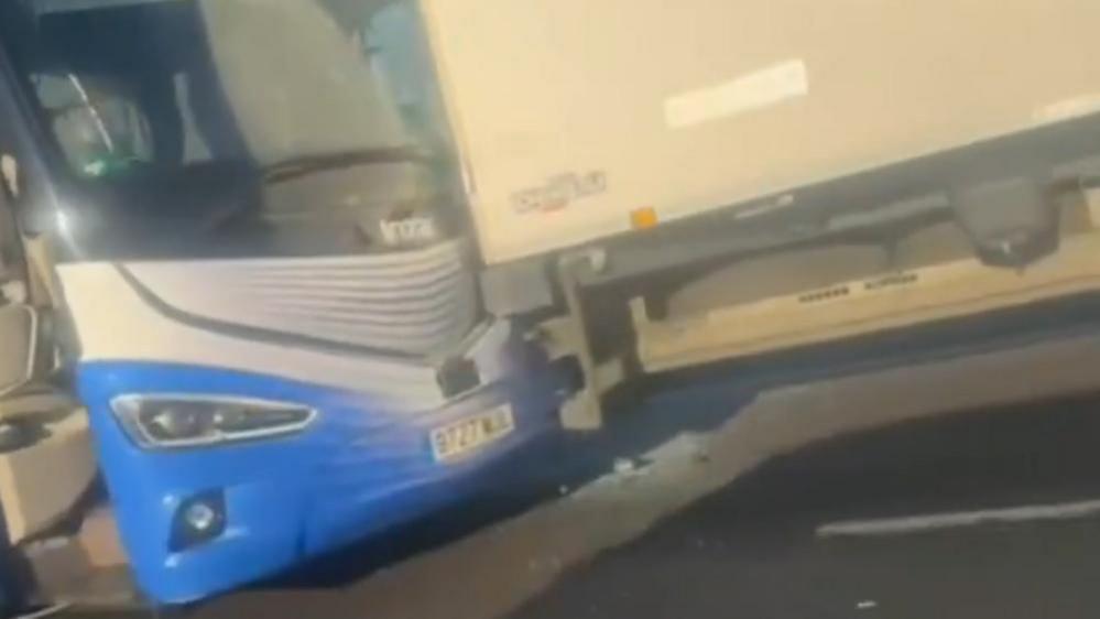 Front of a blue and white coach that has crashed into the back of a white lorry