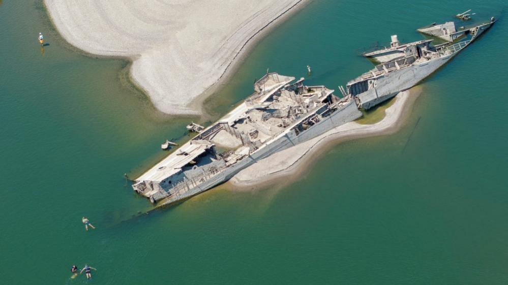 A drone view shows people swimming near a sunken German warship from World War II, exposed due to low Danube River levels caused by drought and extreme heat, in Prahovo, Serbia, July 30, 2026
