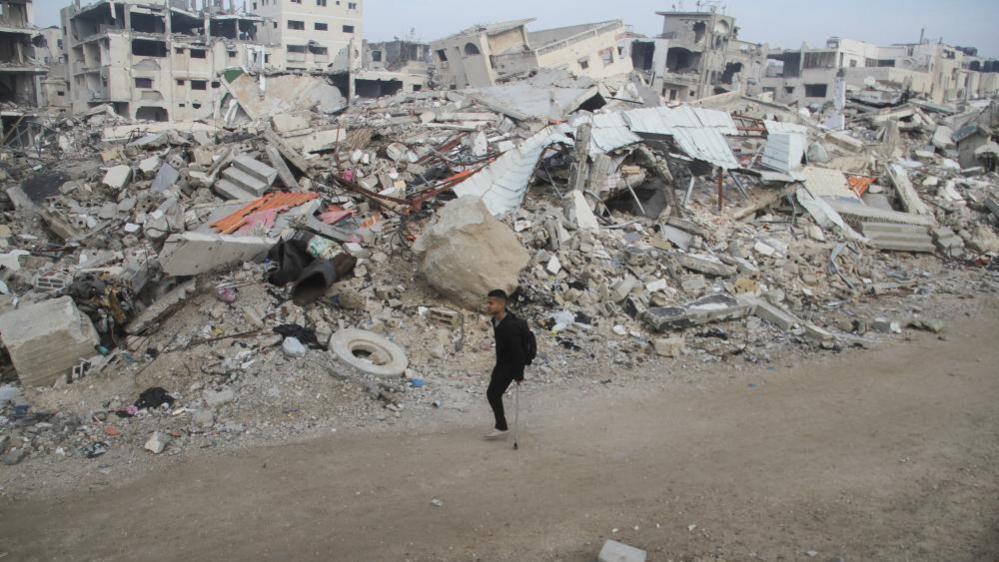 A man with one leg walking on crutches past the ruins of buildings in Gaza