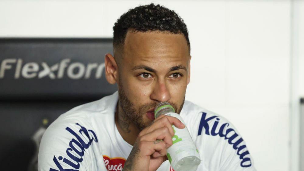 Neymar sitting down drinking from a water bottle