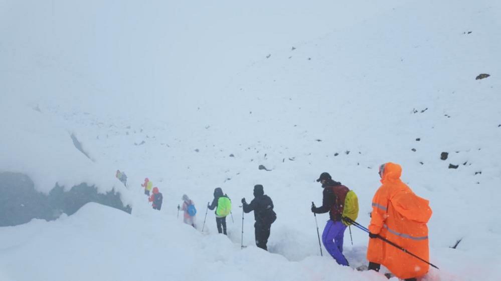 A line of trekkers descends a path covered by snow