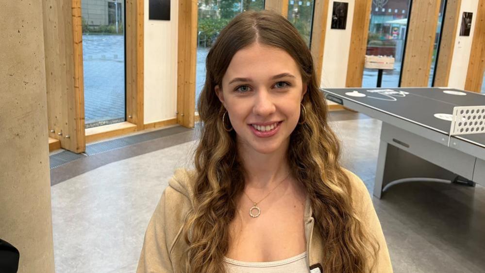 Juliana Skakun with long curly brown hair and a beige top