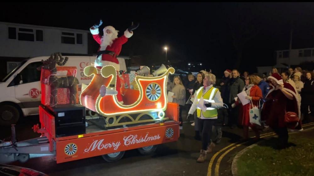 A large group of people follow Santa's sleigh to surprise the family for Christmas.