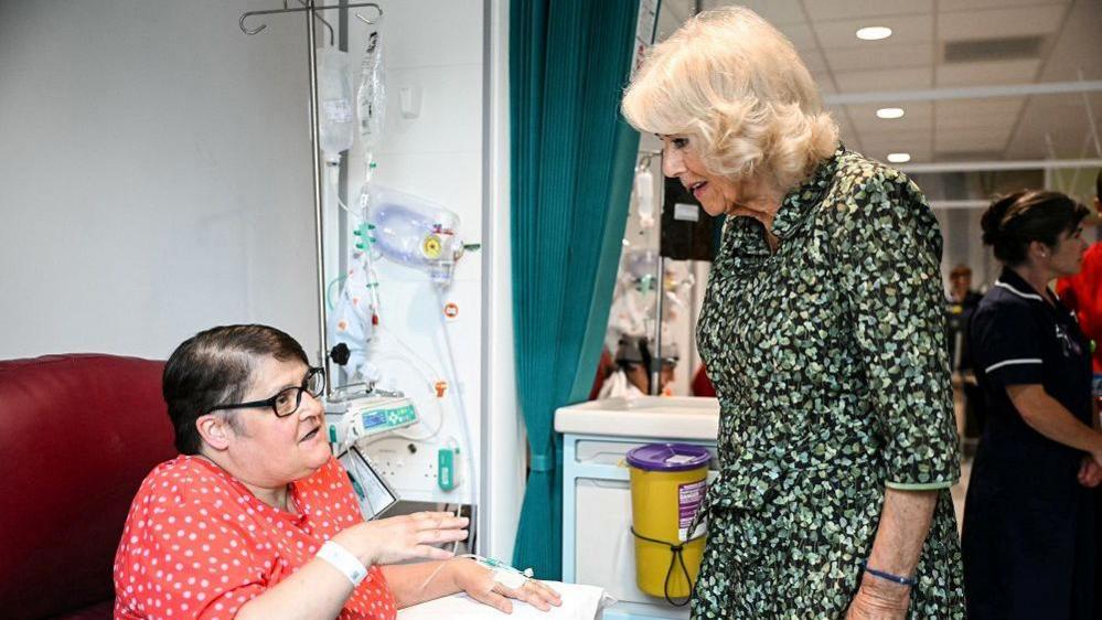 The Queen stands next to a cancer patient who is sitting while getting treatment