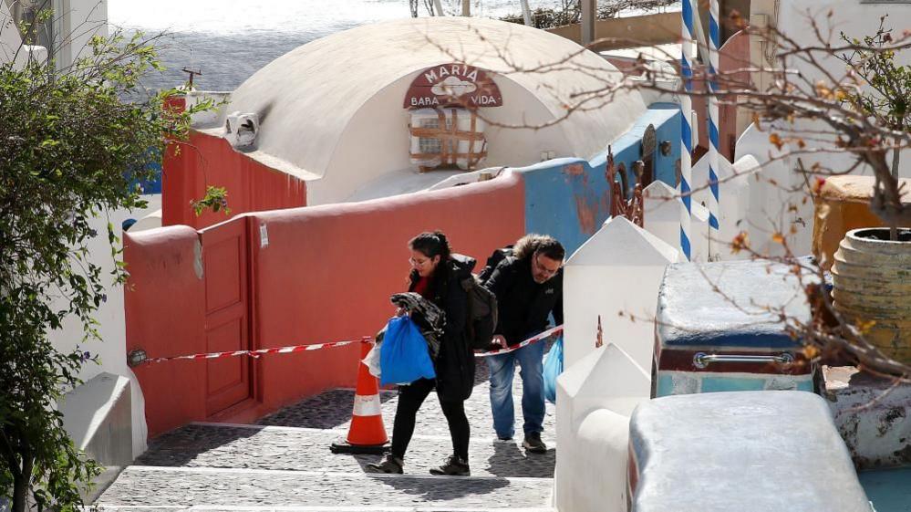 People cross a police cordon as they evacuate their home in the village of Oia on Santorini island, Greece, 05 February 2025