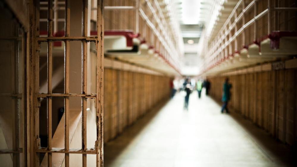 Image shows the corridor of a prison with cells visible
