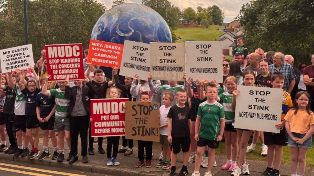 A large group of mainly children holding placards saying stop the stink. They are standing in front of an inflatable globe. 