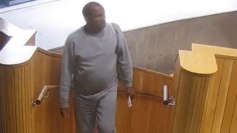 Hadush Kebatu, seen on CCTV, walks ups stairs at a library, surrounded by wood panneling