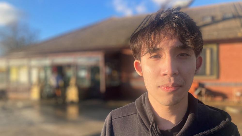 A man in a black hoodie stood in front of a restaurant.