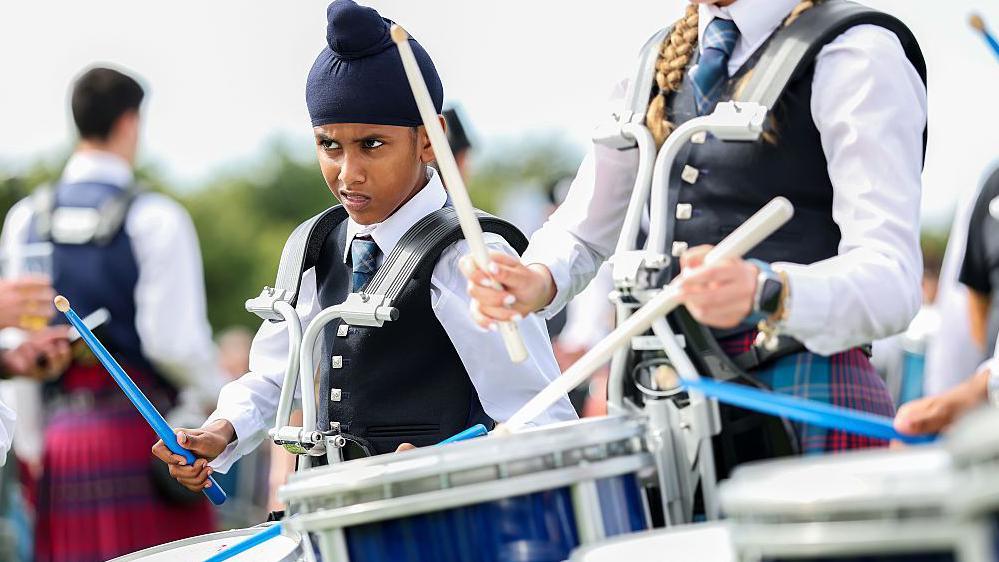 A young boy looking puzzled as he plays a snare drum