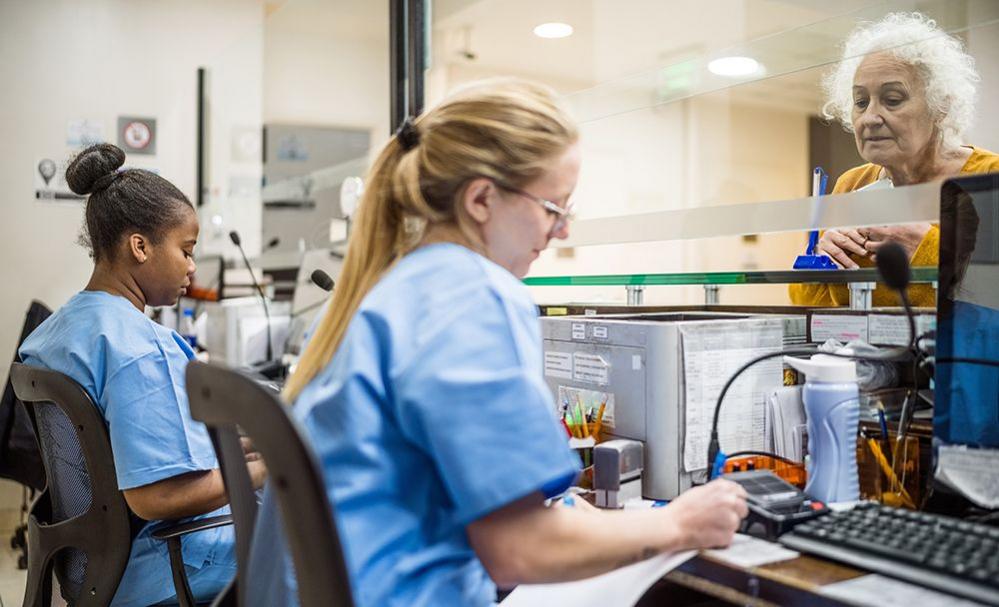 Hospital receptionists work while a woman waits