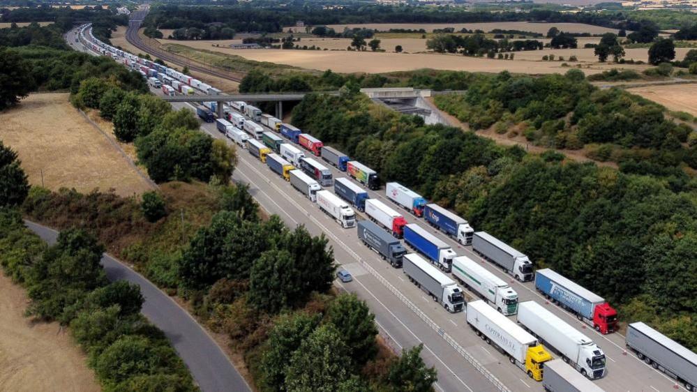 Hundreds of lorries on a motorway. They are queueing heading out of the frame.