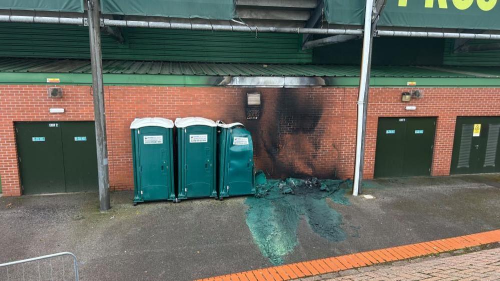 The outside of the Home Park stadium showing smoke damage up the wall and two melted green portable toilets