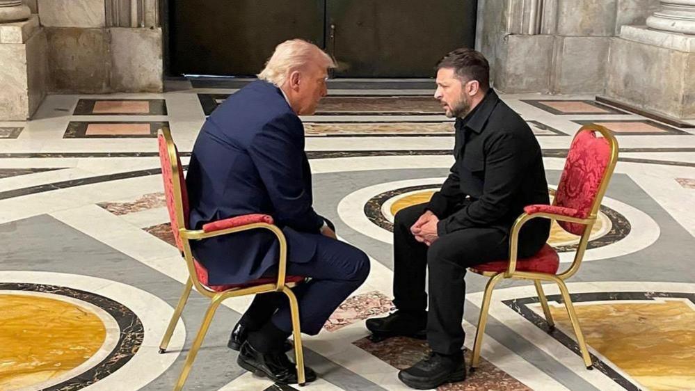 Two men sit on red chairs at St Peter's during the Pope's funeral in April