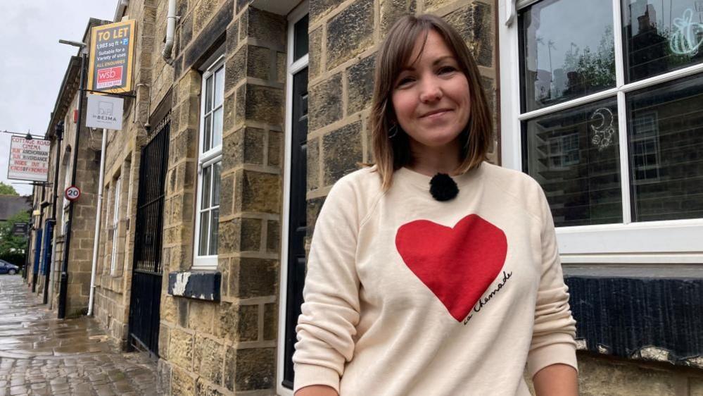 A woman in a sweater standing on a street looking at the camera