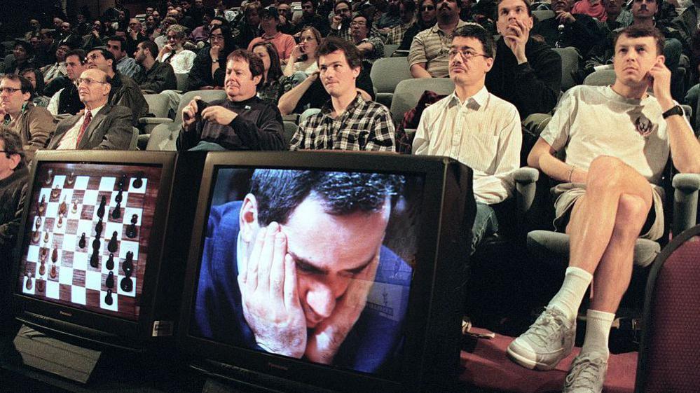 Fans watch a chess game 06 May 1997 in New York between World Chess Champion Garry Kasparov (on TV monitor) and the IBM Deep Blue computer. The game was televised from the playing room to this auditorium where chess experts analyzed each move. 