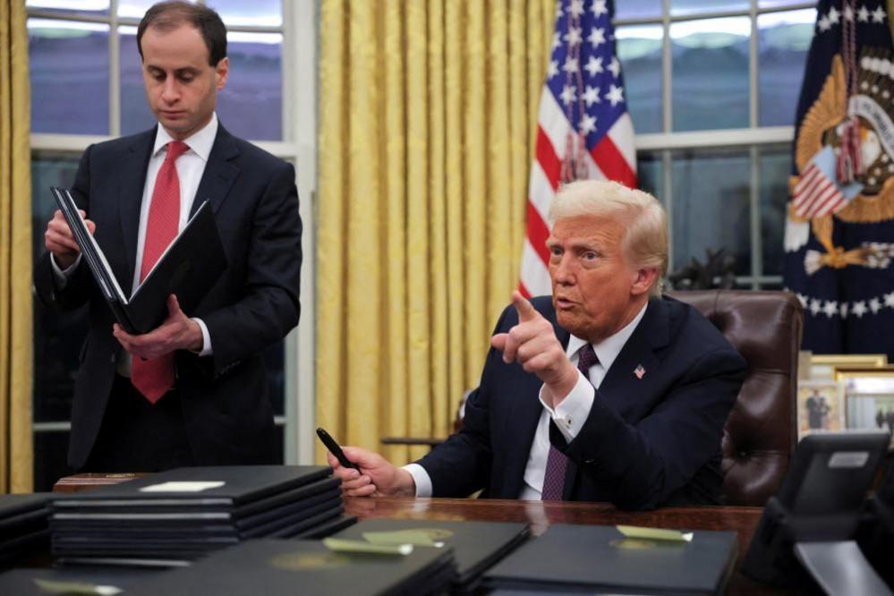 Donald Trump sitting at a desk in the Oval Office as he signs executive orders