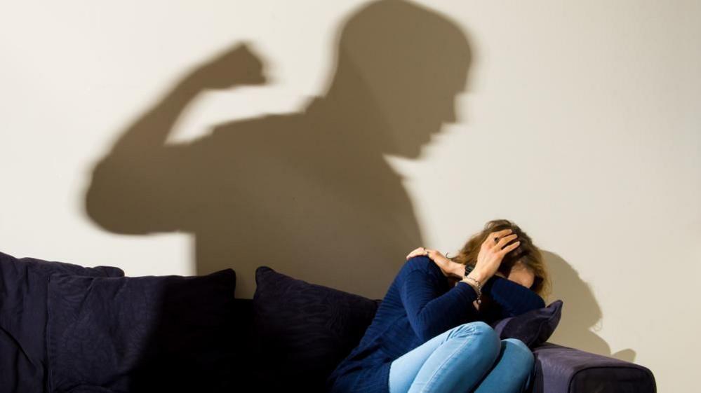 Library pictures of woman cowering on sofa with shadow of man with clenched fist behind her