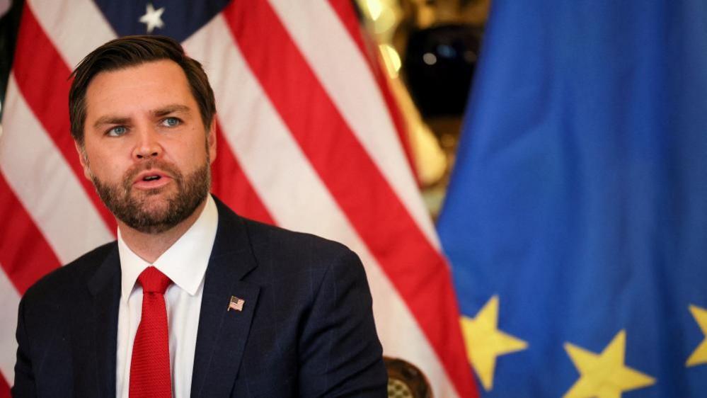 JD Vance in front of US and EU flags