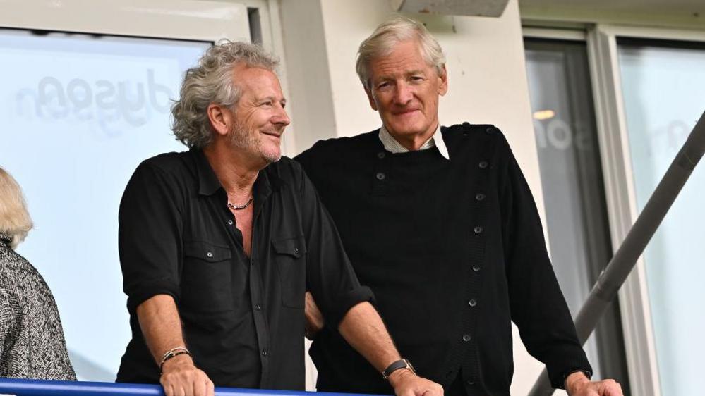 Sir James Dyson and Bruce Craig lean on a balcony at The Rec at a Bath Rugby game together