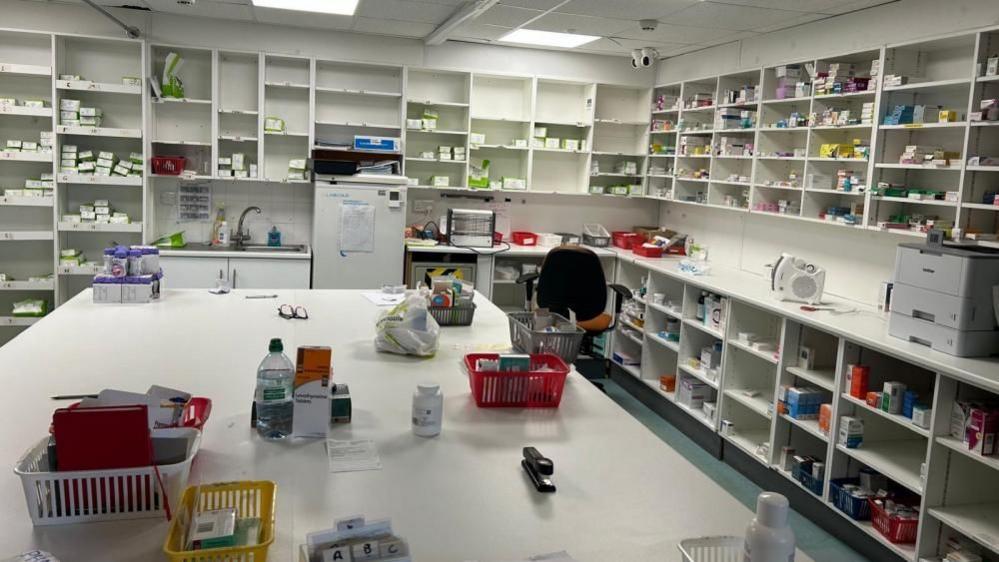 The photo shows dozens and dozens of boxes of medication left on shelves inside the pharmacy after Jhoots were asked to leave. More medication, note books and baskets full of other items can also be seen on a large white table in the middle of the room.