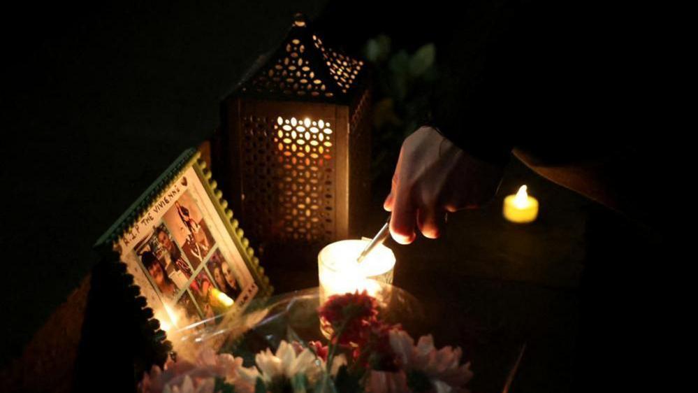 The image shows a person lighting a candle during a vigil for James Lee Williams, popularly known as The Vivienne, in Liverpool, Britain, on 12 January, 2025
