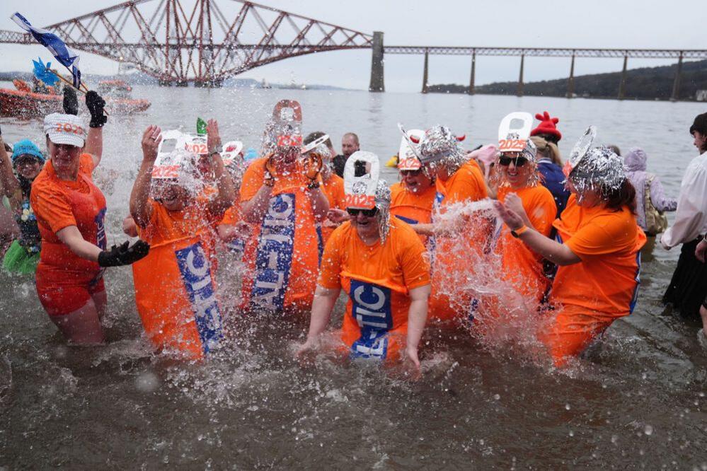 People dressed up in Irn bru outfits with 2025 hats splash about in the Firth of Forth.